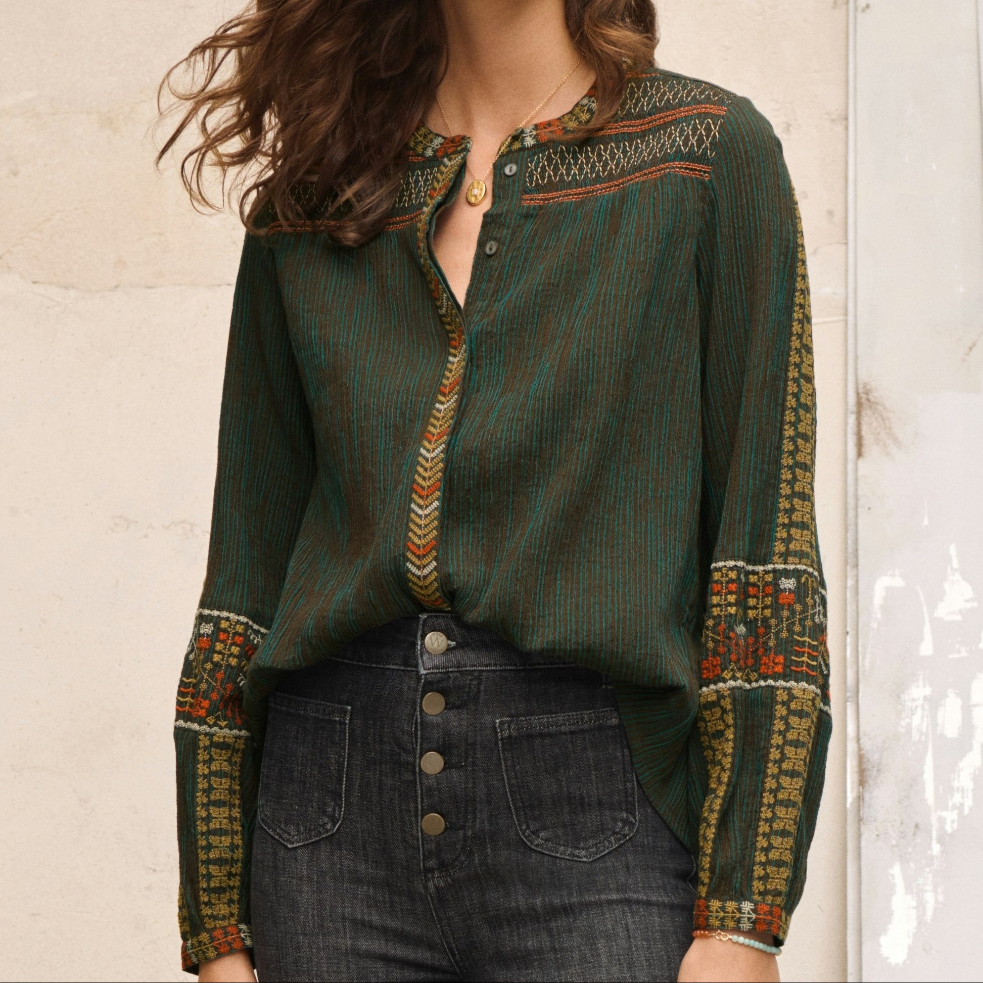 Woman wearing a green blouse with patterned sleeves against a neutral background