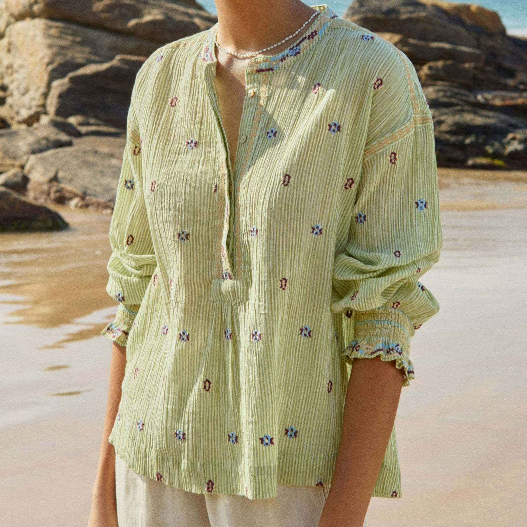 Woman wearing a light green blouse with floral patterns on a beach.