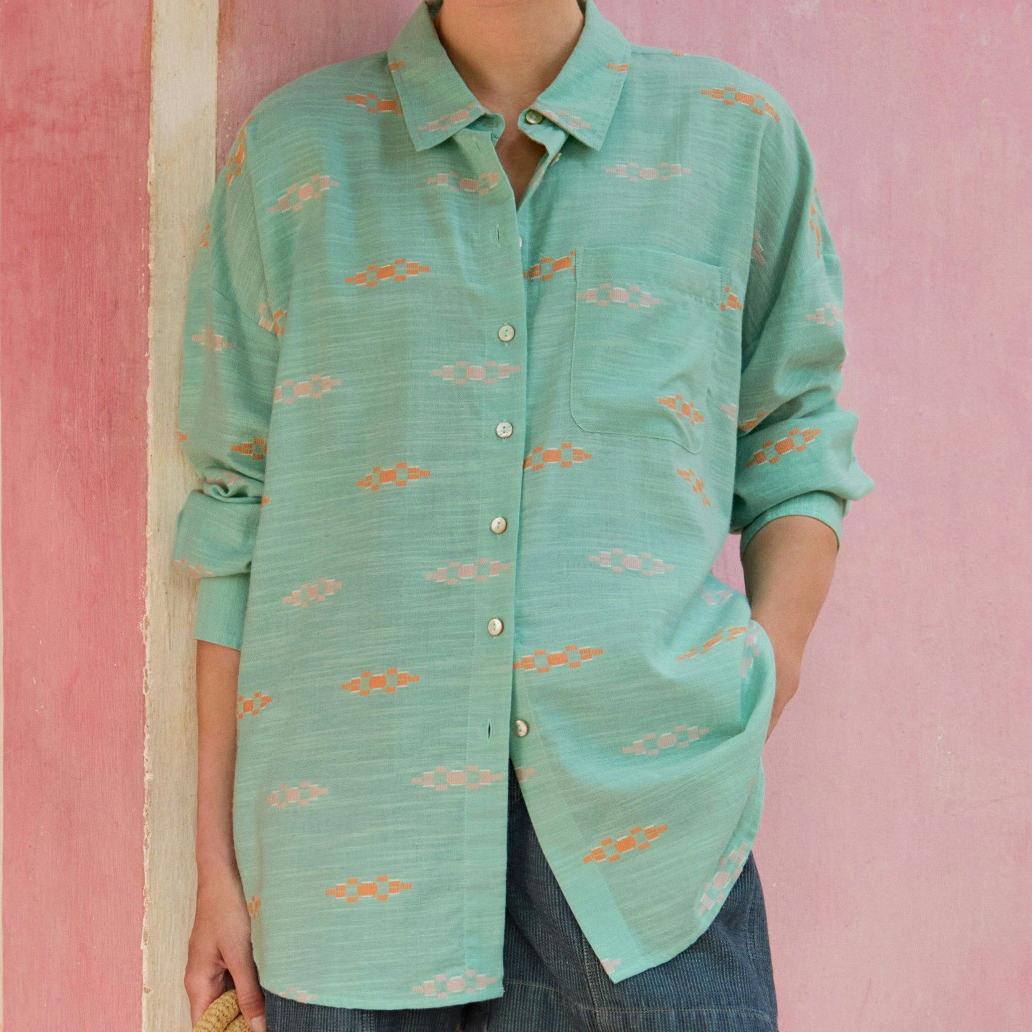 Woman wearing a teal patterned shirt against a pink wall