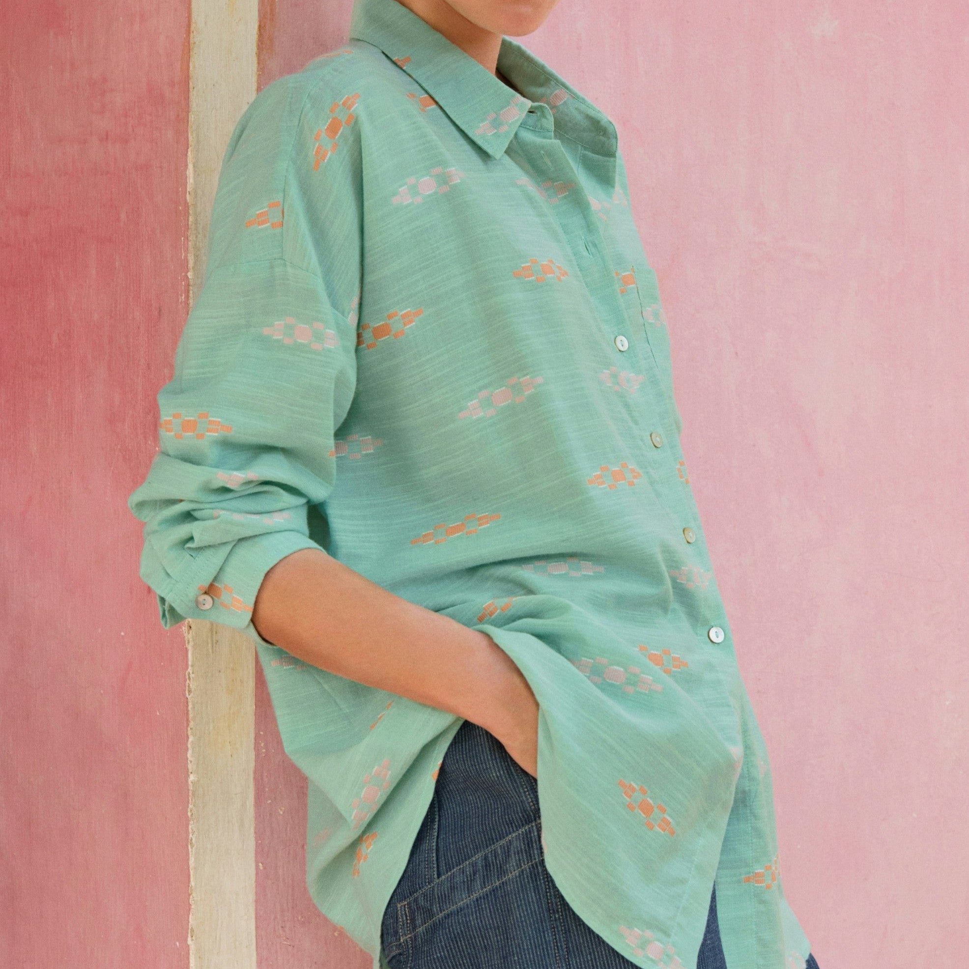 Woman wearing a light green patterned shirt against a pink wall