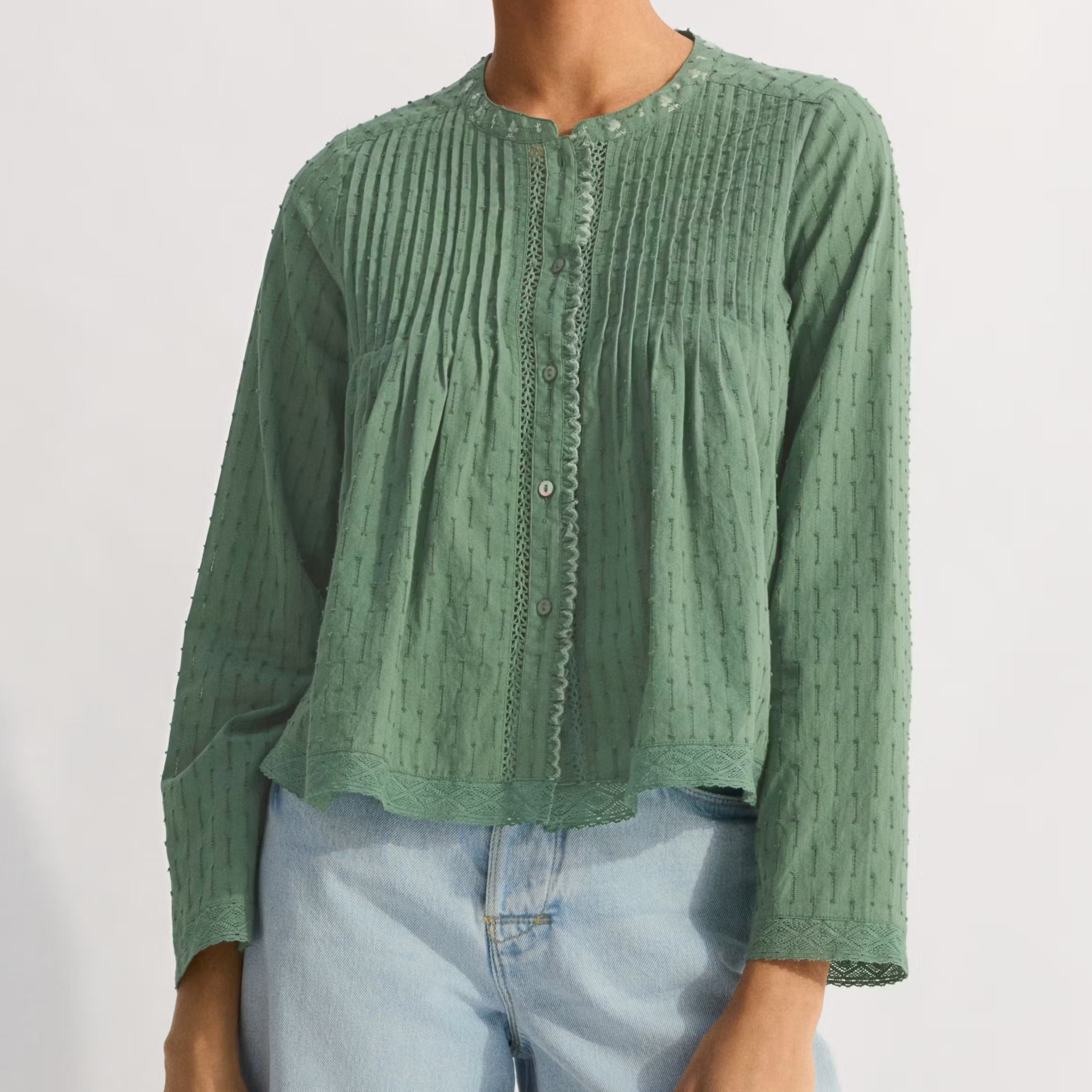 Woman wearing a green textured blouse and light blue shorts on a white background