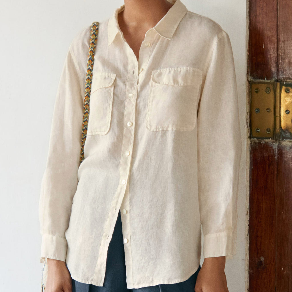 Woman wearing a beige shirt and blue pants standing against a white wall.