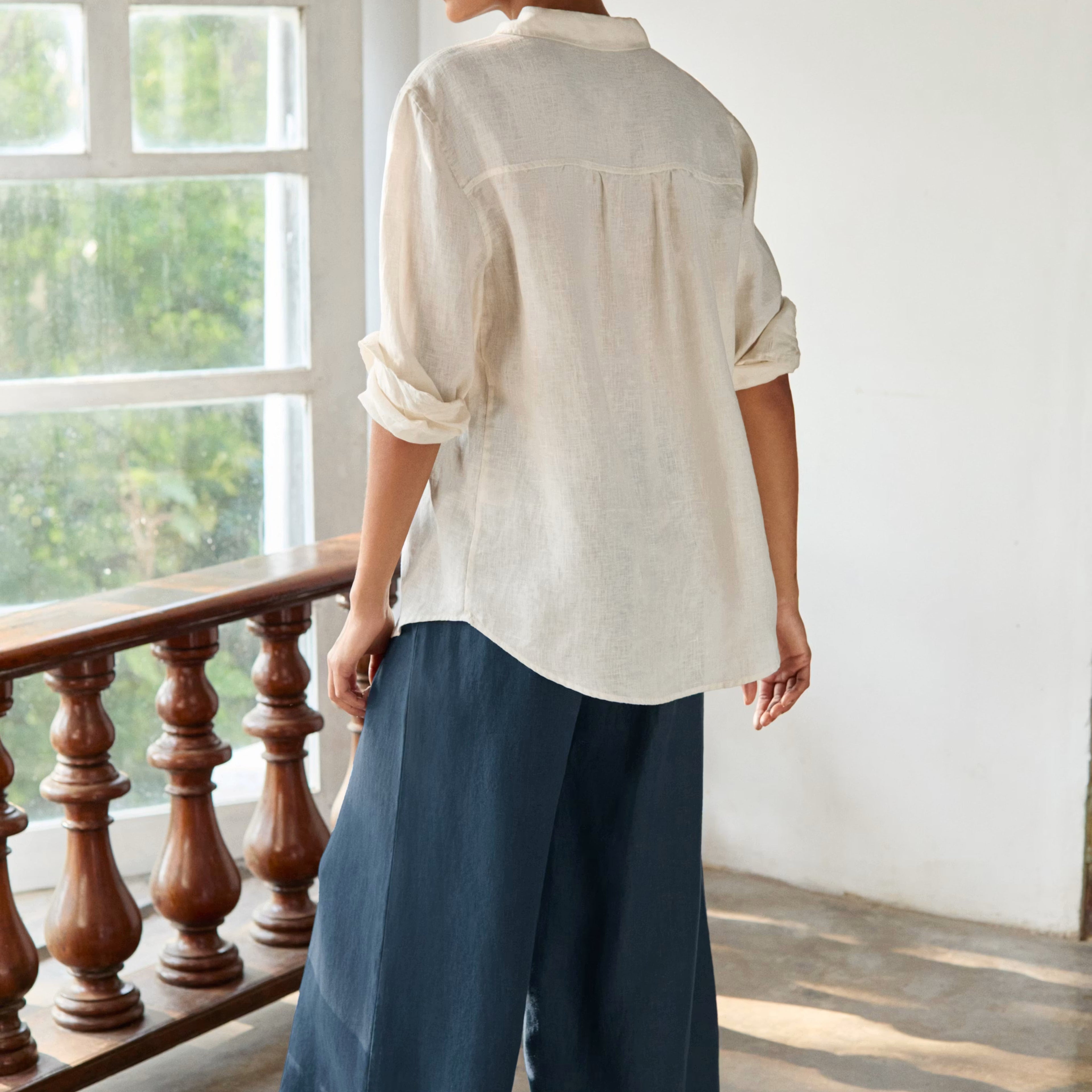 Woman wearing a white shirt and blue pants standing in a room with large windows.