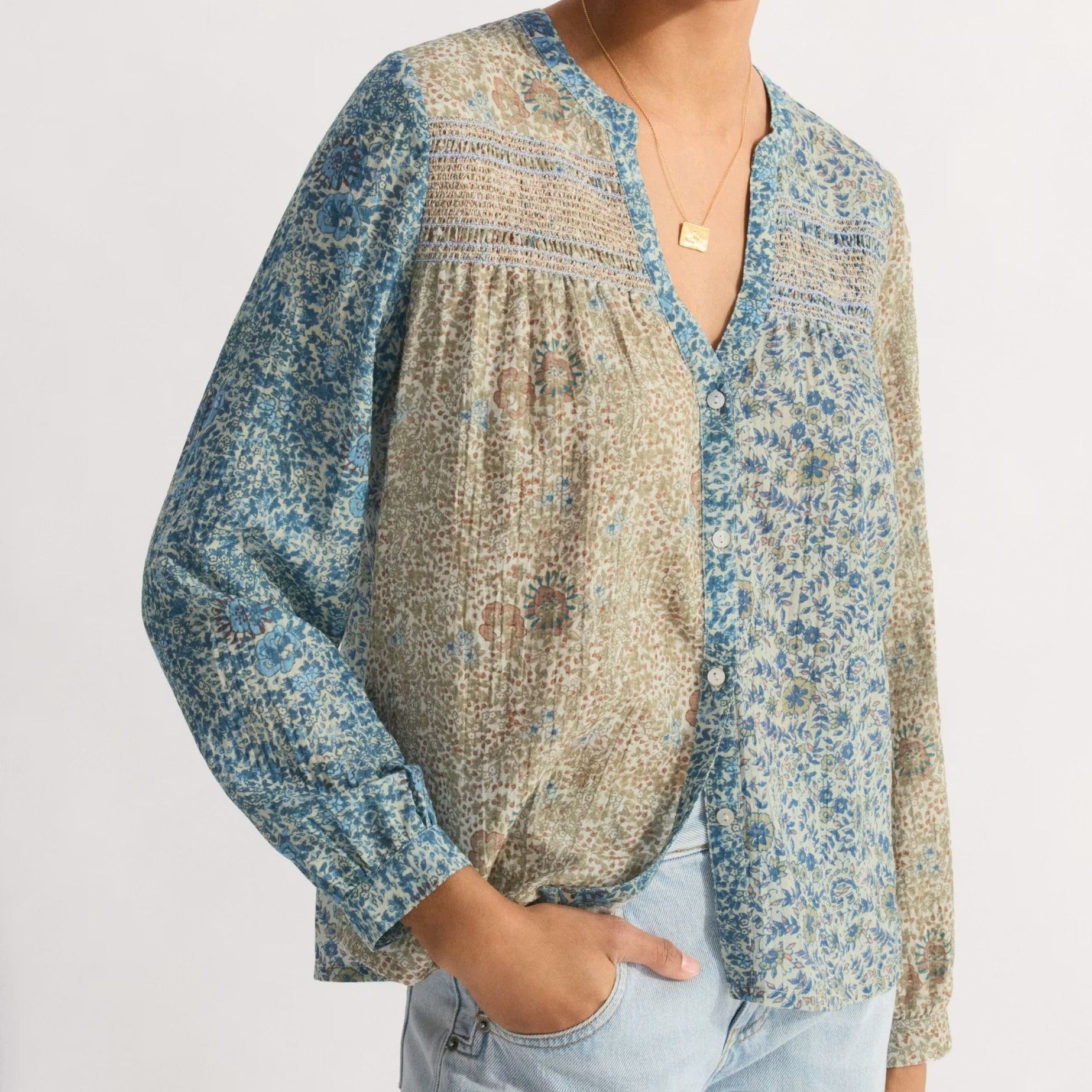 Woman wearing a patterned blouse and light blue jeans on a white background