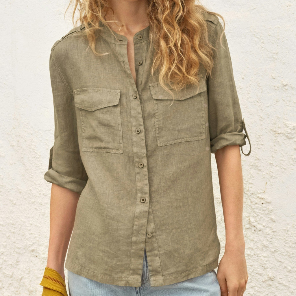 Woman wearing an olive green shirt with rolled-up sleeves against a textured wall.