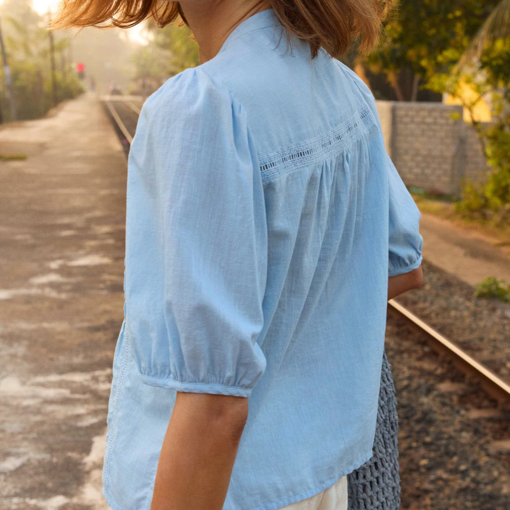 Woman wearing a light blue blouse standing on a path with greenery in the background